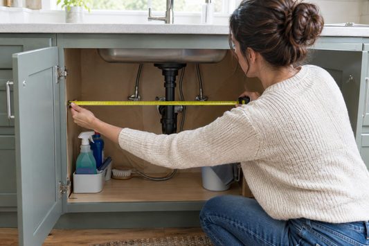 omeowner measuring usable interior width inside an open under-sink kitchen cabinet